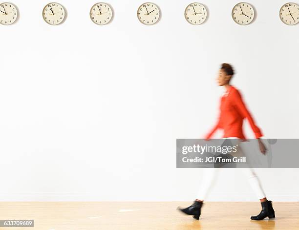 mixed race businesswoman walking under clocks - blurred motion foto e immagini stock