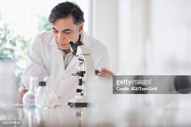 mixed race scientist using microscope in laboratory - nur erwachsene stock-fotos und bilder