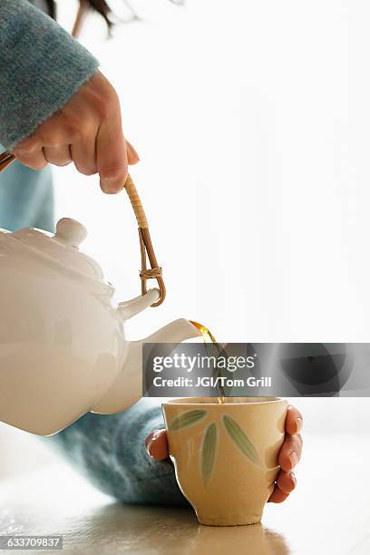 hispanic woman pouring cup of tea - theepot stockfoto's en -beelden
