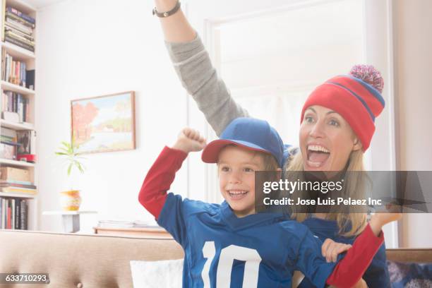 mother and son watching sports in living room - woman in sports jersey stock pictures, royalty-free photos & images