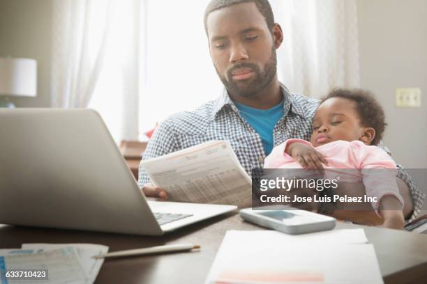 father holding baby daughter and working from home - family budget imagens e fotografias de stock