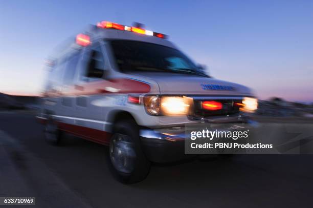 blurred view of ambulance driving at dusk - ambulance stockfoto's en -beelden