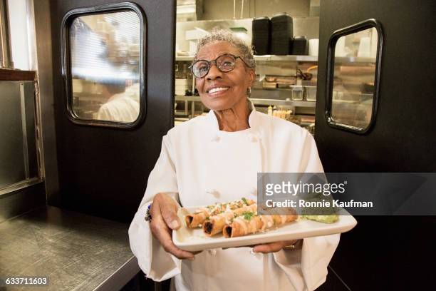 black chef holding plate of food in restaurant - black chef stock pictures, royalty-free photos & images