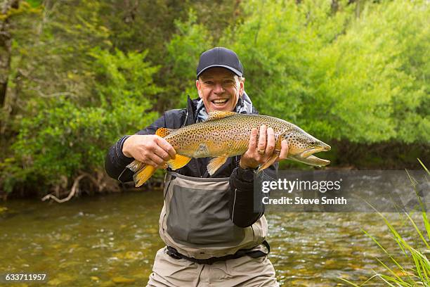 caucasian man holding fish in remote river - fly fishing foto e immagini stock