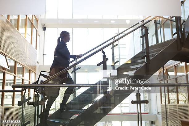 woman walking up stairs in office building - escalón y escalera fotografías e imágenes de stock