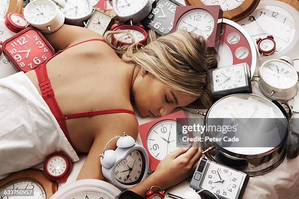 young woman asleep on pile of clocks - overslept stockfoto's en -beelden