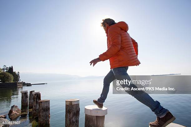 man hops between dock posts above tranquil lake - orange jacket stock pictures, royalty-free photos & images