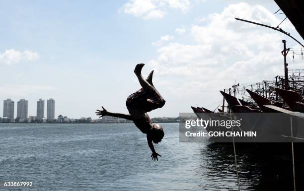 An Indonesian boy jumps into the sea from a pier at the main fishing port of Muara Angke to cool off in Jakarta on February 5, 2017. / AFP PHOTO /...