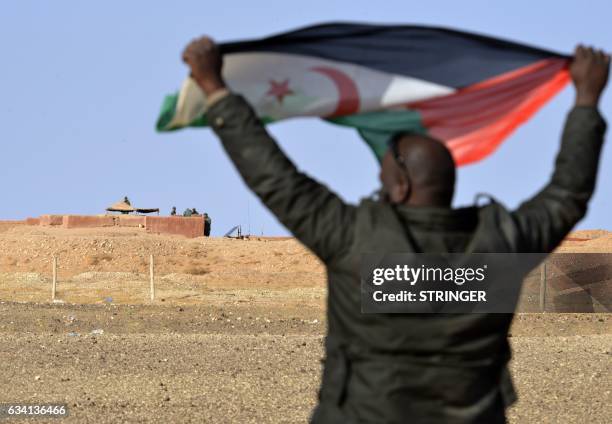 Saharawi man holds up a Polisario Front flag in the Al-Mahbes area near Moroccan soldiers guarding the wall separating the Polisario controlled...