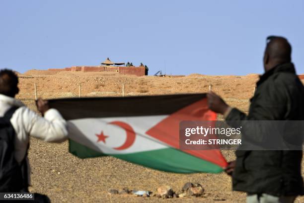 Saharawi men hold up a Polisario Front flag in the Al-Mahbes area near Moroccan soldiers guarding the wall separating the Polisario controlled...