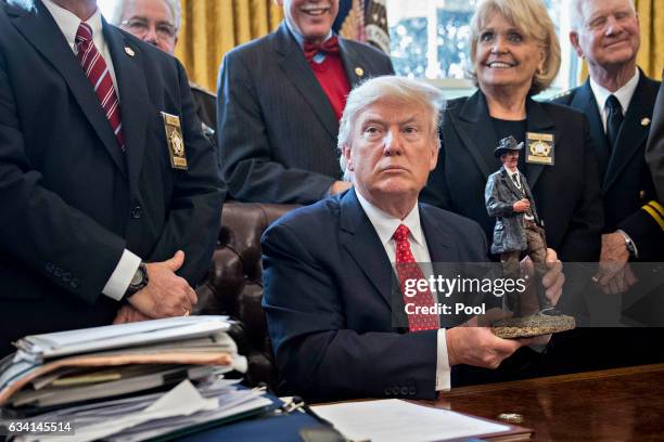 President Donald Trump holds up a statue he received as a gift while meeting with county sheriffs in the Oval Office of the White House on February...