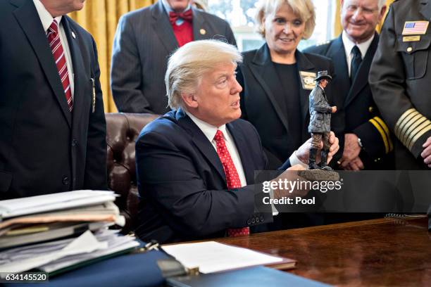 President Donald Trump holds up a statue he received as a gift while meeting with county sheriffs in the Oval Office of the White House on February...