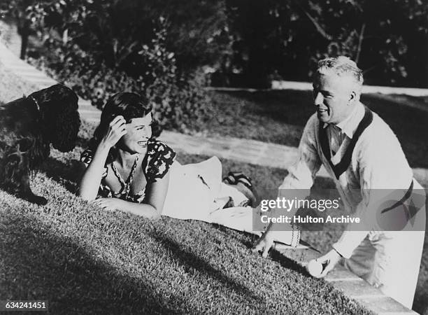 English comic actor and filmmaker Charlie Chaplin and his wife, actress Paulette Goddard playing with their cocker spaniel, circa 1940.