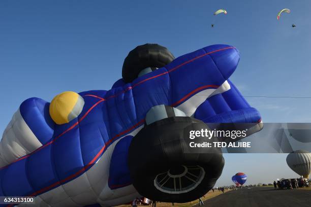 Balloon in the shape of a race car is inflated as powered paragliders are seen in flight during the annual International Hot Air Balloon Festival at...
