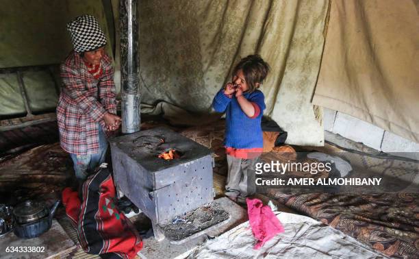 Displaced Syrian girls warm themselves by a stove at a refugee camp in the eastern Ghouta region on the outskirts of the capital Damascus on February...