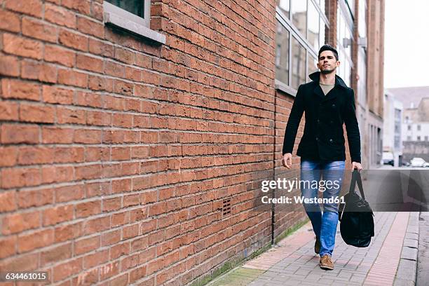 young casual businessman walking in the street, carrying bag - caban photos et images de collection