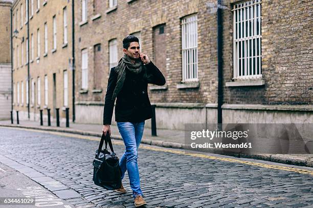 young casual businessman walking in the street using mobile phone - caban photos et images de collection