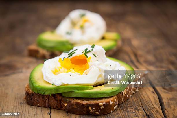 wholemeal bread slices with sliced avocado and poached eggs on wood - escalfado fotografías e imágenes de stock