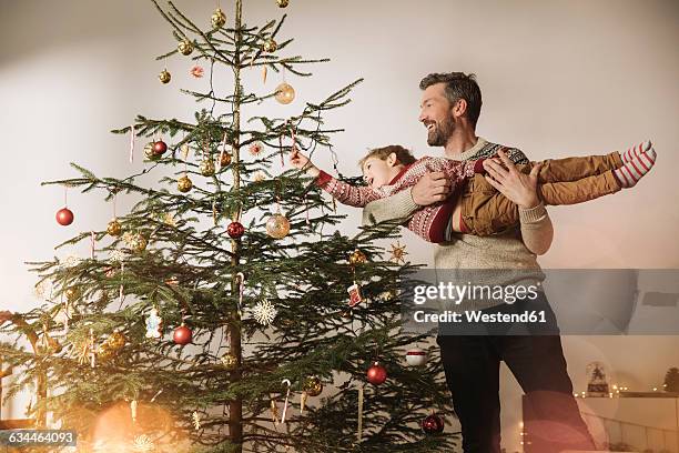 father and son decorating christmas tree - decorare l'albero di natale foto e immagini stock