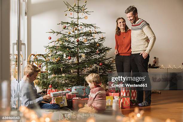 happy parents watching their children unwrap christmas gifts - gift lounge stock pictures, royalty-free photos & images