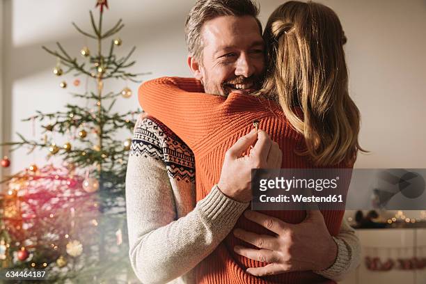 couple hugging after engagement by christmas tree - man proposing indoor stock-fotos und bilder