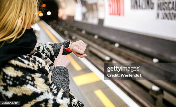 young woman looking on her smartwatch waiting for the subway - auf die uhr schauen stock-fotos und bilder