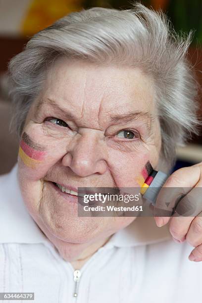 portrait of confident senior woman painting german national colors on her cheek - faces of a nation stock pictures, royalty-free photos & images