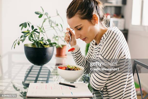 woman sitting at table with fruit muesli looking at notepad - diet journal - fotografias e filmes do acervo