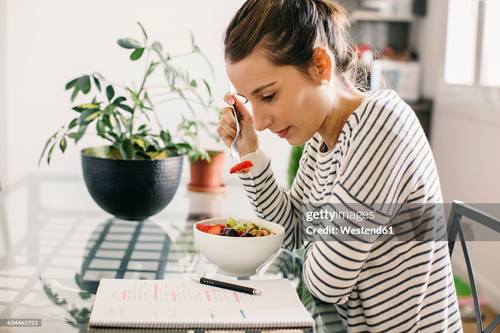 Woman sitting at table with fruit muesli looking at notepad