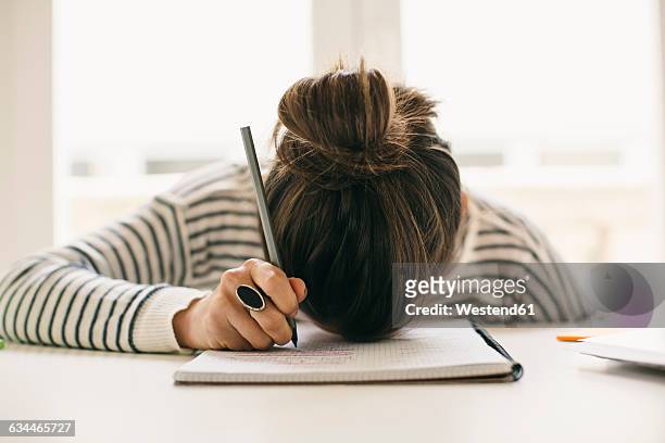 woman writing on notepad resting her head on table - frustrazione foto e immagini stock