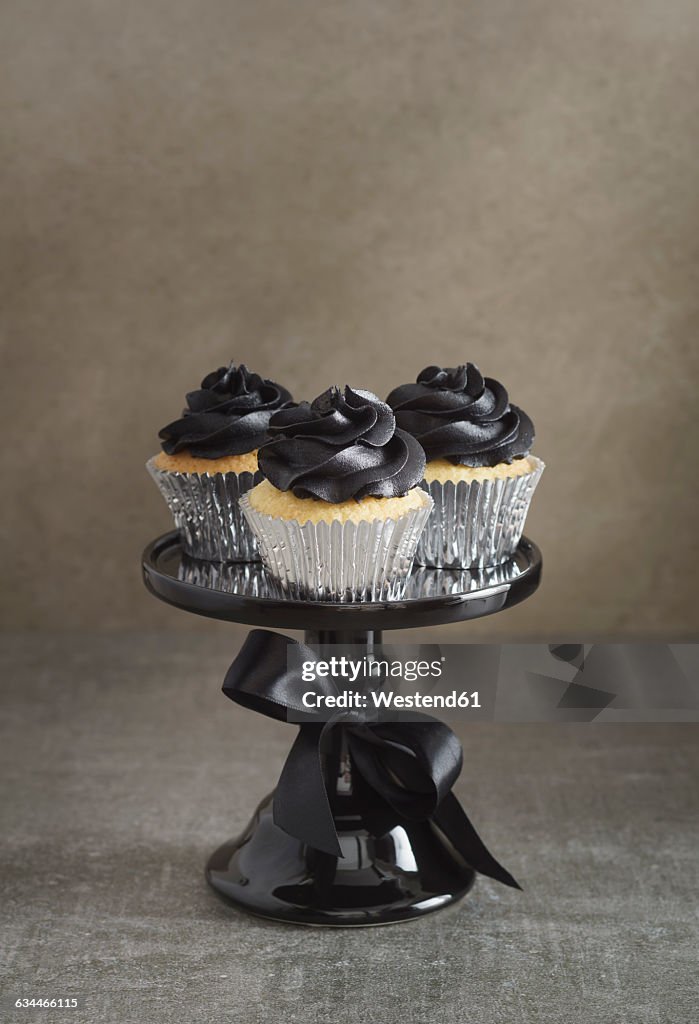 Three cup cakes with black buttercream topping on a cake stand