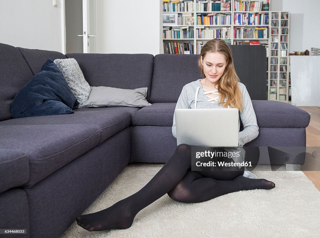 Young woman sitting on the floor of living room using laptop