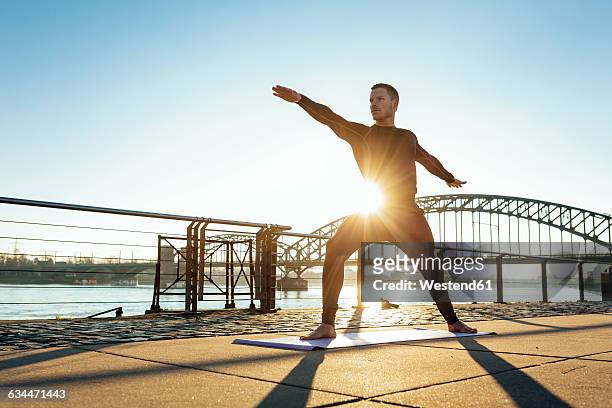 germany, cologne, young man practicing yoga at the riverside - man doing yoga in the morning stockfoto's en -beelden