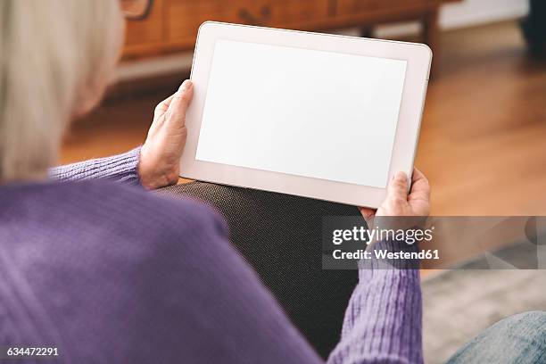 over the shoulder shot of elderly woman using a tablet computer at home - one senior woman only stock pictures, royalty-free photos & images