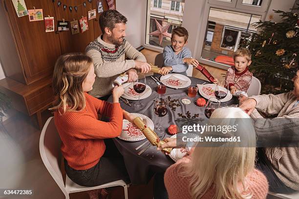 happy family of three generations pulling at ends of christmas crackers before dinner - christmas crackers stock pictures, royalty-free photos & images