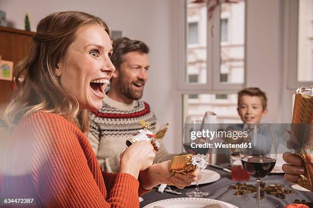 happy woman pulling christmas cracker at family table - christmas surprise stock pictures, royalty-free photos & images