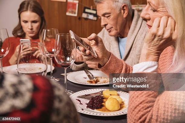family members playing with their smartphones after christmas dinner - smartphone table stockfoto's en -beelden