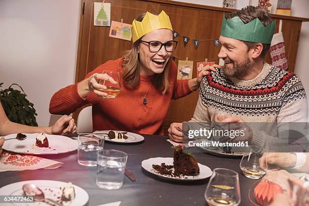 happy couple with paper crowns laughing while having christmas dinner - christmas pudding stockfoto's en -beelden