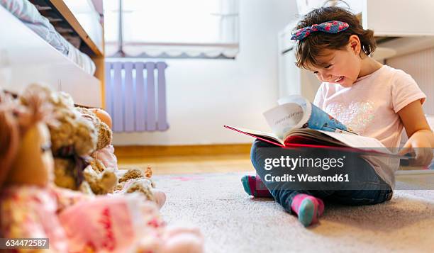 laughing little girl sitting on the floor watching picture book - 2 year old book stock pictures, royalty-free photos & images