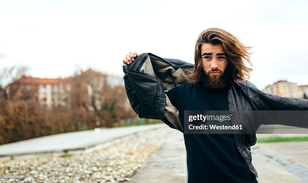 Portrait of bearded young man putting on his leather jacket