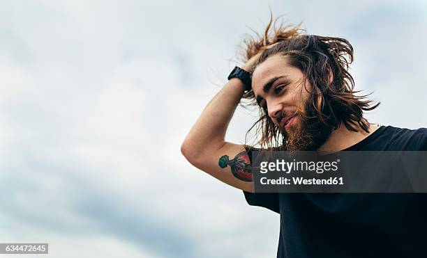 portrait of bearded young man with tattoo on his upper arm - haare mann stock-fotos und bilder