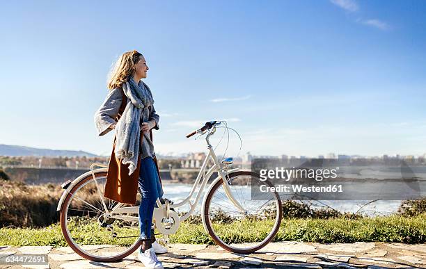 spain, gijon, smiling young woman on bicycle at the coast - asturien stock-fotos und bilder