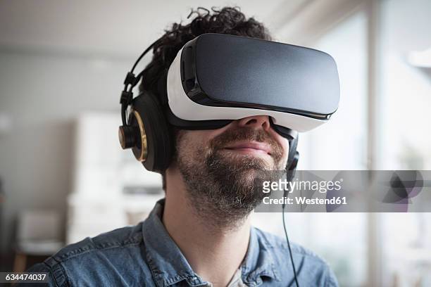 smiling man wearing virtual reality glasses and headphones - casques réalité virtuelle photos et images de collection