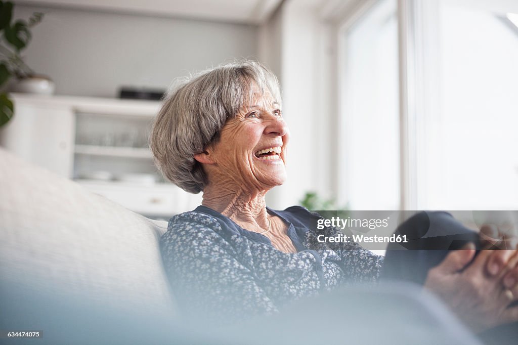 Portrait of laughing senior woman sitting on couch at home