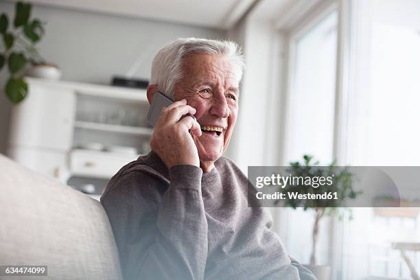 portrait of laughing senior man telephoning with smartphone at home - senior men laughing stock pictures, royalty-free photos & images