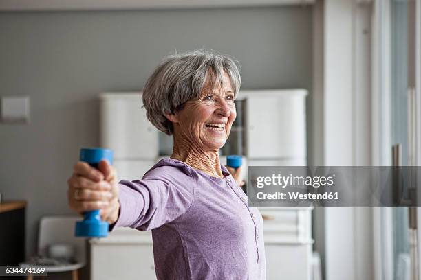 portrait of happy senior woman doing fitness exercise with dumbbells at home - old people sport foto e immagini stock
