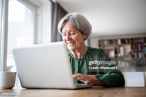 portrait of senior woman using laptop at home - septuagénaire photos et images de collection