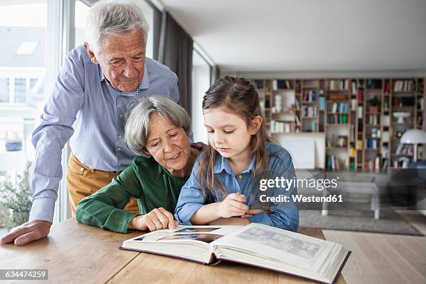 grandparents watching photo album with their granddaughter at home - looking at a photo album stock-fotos und bilder