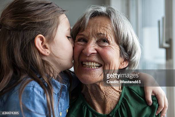 little girl kissing her grandmother - seniorinnen stock-fotos und bilder