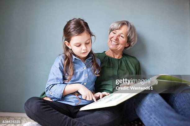 happy grandmother and her granddaughter sitting on the floor with a book - reading old young stock pictures, royalty-free photos & images